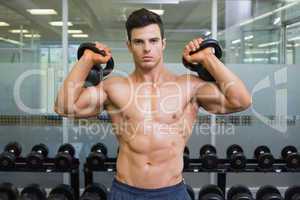 Muscular man lifting kettle bells in gym