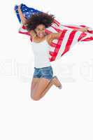 Pretty girl wrapped in american flag jumping and smiling at came