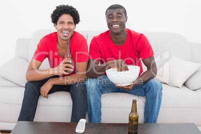 Football fans in red sitting on couch with beer and popcorn