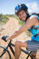 Fit man cycling up mountain trail smiling at camera