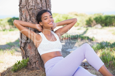 Fit woman sitting against tree smiling