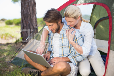 Attractive couple sitting by their tent using laptop