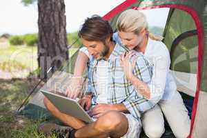 Attractive couple sitting by their tent using laptop