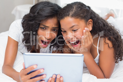 Surprised mother and daughter using tablet together