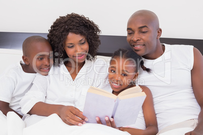 Happy family reading book together in bed