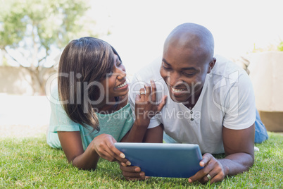 Happy couple lying in garden using tablet pc together