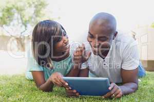 Happy couple lying in garden using tablet pc together