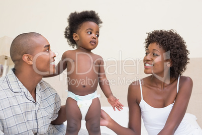 Happy couple sitting on bed with baby daughter