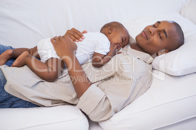 Happy father napping with baby son on couch