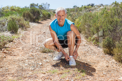 Smiling jogger tying his shoelace on mountain trail