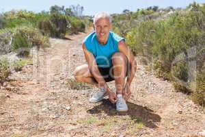 Smiling jogger tying his shoelace on mountain trail