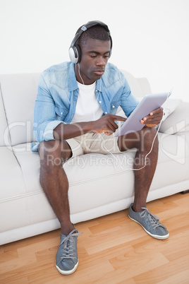 Casual man sitting on sofa using his tablet pc to listen to musi