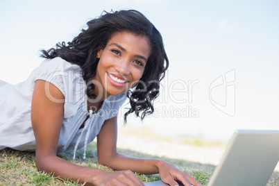 Casual pretty woman lying on the grass using her laptop