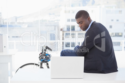Serious businessman sitting on desk looking at laptop