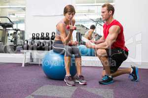 Personal trainer with client sitting on exercise ball lifting du