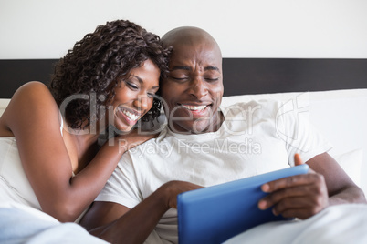 Happy couple cuddling in bed with tablet pc