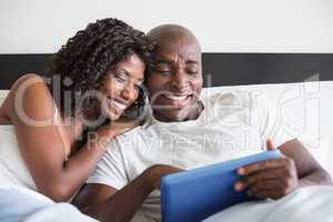 Happy couple cuddling in bed with tablet pc