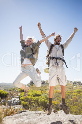 Hiking couple standing on mountain terrain cheering and jumping