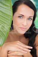 Beautiful nude brunette smiling at camera with green leaf