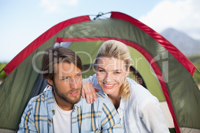 Attractive happy couple sitting by their tent smiling at camera