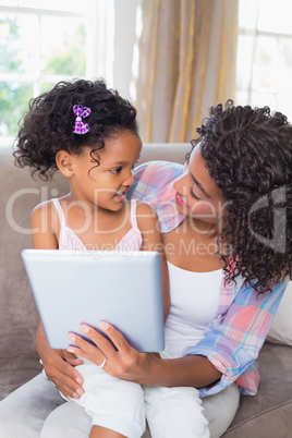 Pretty mother sitting on couch with cute daughter using tablet t