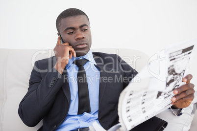 Businessman making a call while reading the paper on sofa