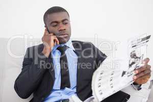 Businessman making a call while reading the paper on sofa