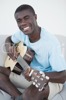 Casual man sitting on sofa playing the guitar