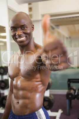 Shirtless muscular man giving thumbs up in gym