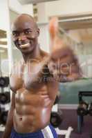 Shirtless muscular man giving thumbs up in gym