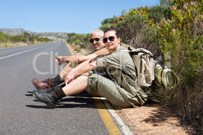 Hiking couple sitting on the side of the road smiling at camera