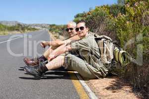 Hiking couple sitting on the side of the road smiling at camera