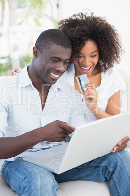 Attractive couple using laptop together on sofa to shop online