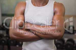 Mid section of a muscular man with arms crossed in gym
