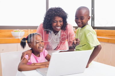 Cute siblings using laptop together with mother