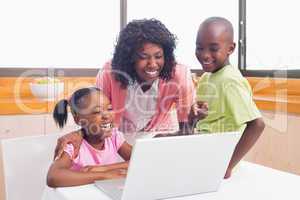 Cute siblings using laptop together with mother