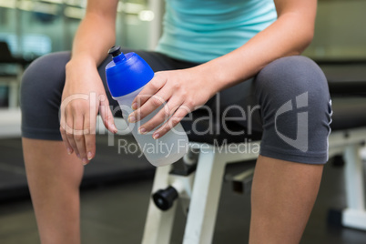 Fit woman sitting on bench holding sports bottle