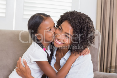 Pretty mother sitting on the couch with her daughter kissing her