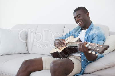 Casual man sitting on sofa playing the guitar