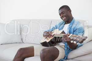 Casual man sitting on sofa playing the guitar