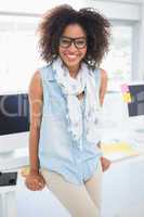 Pretty designer smiling at camera leaning on desk