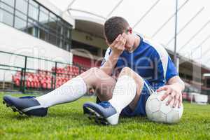 Disappointed football player in blue sitting on pitch after losi