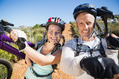 Active couple carrying their bikes on country terrain together