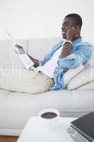 Casual man lying on sofa on the phone holding newspaper