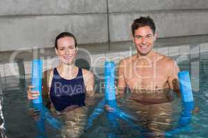 Happy couple holding foam rollers smiling at camera