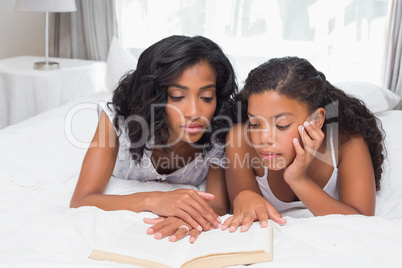 Mother and daughter reading book together on bed