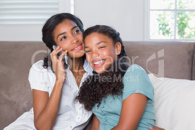 Happy mother and daughter using smartphone together on sofa