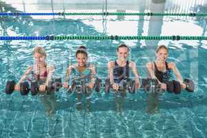 Smiling female fitness class doing aqua aerobics with foam dumbb