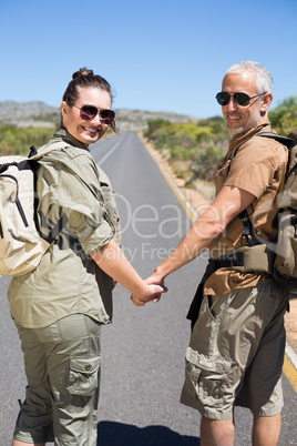 Hitch hiking couple holding hands on the road smiling at camera