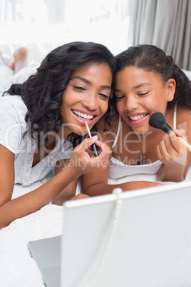 Smiling mother and daughter using laptop together on bed putting